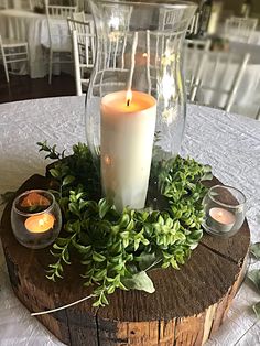 a candle is sitting on top of a wooden slice with greenery and candles in it