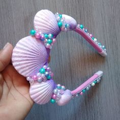 a hand is holding a pink and blue hair comb with pearls, beads and seashells on it