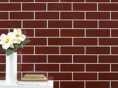 a white vase filled with flowers sitting on top of a table next to a red brick wall