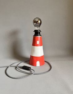 a red and white lighthouse shaped lamp on a cord