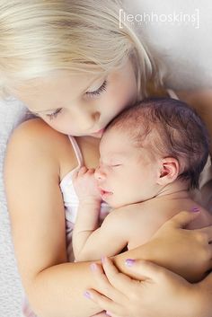 a woman holding a baby in her arms while laying on top of a bed with white sheets