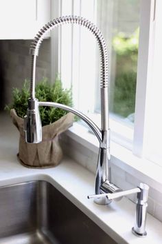 a kitchen sink and faucet in front of a window with potted plants