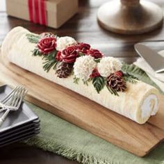 a wooden table topped with a roll of cake covered in frosting and flowers on top of it