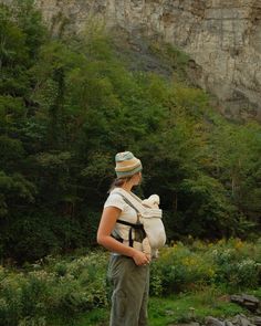 a woman with a baby strapped to her back is standing in front of a mountain