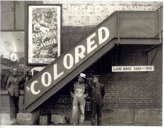 an old black and white photo of people standing under a sign that reads, colored