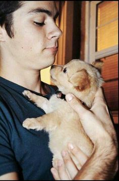 a young man holding a puppy in his arms and kissing it's face with its eyes closed