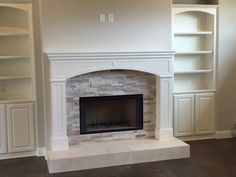 an empty living room with a fireplace and built - in bookshelves