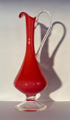 a red glass vase sitting on top of a table next to a white wall and floor