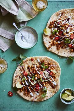 two pita breads with various toppings on a green tray next to some dipping sauce