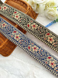 two blue and gold patterned ribbon next to flowers on a white table with wicker basket in the background