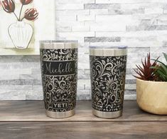 two personalized tumblers sitting on top of a wooden table next to a potted plant