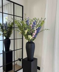 two black vases filled with flowers sitting on top of a wooden table next to a mirror