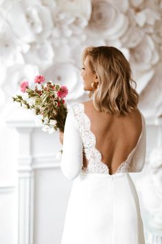 the back of a woman in a white wedding dress holding a bouquet of pink flowers