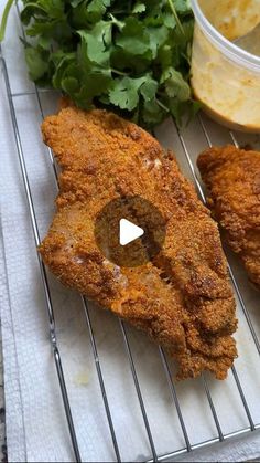 some fried food is sitting on a cooling rack next to greens and dipping sauces