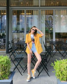 a woman in yellow jacket and shorts posing for the camera with her hand on her head