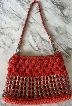 an orange crocheted purse sitting on top of a marble counter next to a metal chain