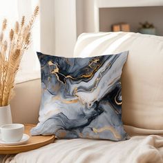 a white couch with a blue and gold pillow sitting on top of it next to a cup