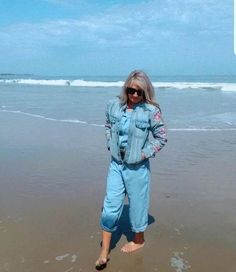 a woman is standing on the beach with her feet in the sand and wearing sunglasses