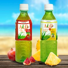 two bottles of alo juice next to some fruit on a table with the ocean in the background