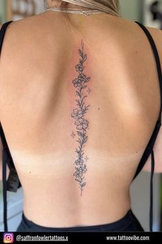 the back of a woman's neck with flowers and leaves tattooed on her lower back