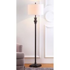 a floor lamp with a white shade on it and a gray chair in the background