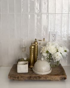 white flowers in a glass vase on a wooden tray next to a faucet and soap dispenser