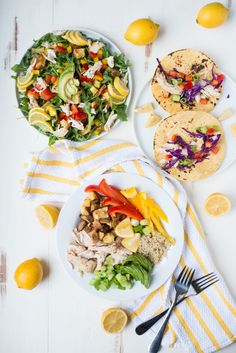 two plates of food on a white table with lemons and forks next to them