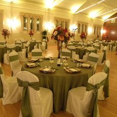 a banquet hall with tables and chairs covered in green cloths, decorated with flowers