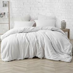 a bed with white linens and pillows in a room next to a brick wall