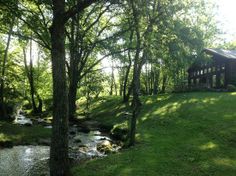 a house sitting on top of a lush green hillside next to a river in the forest