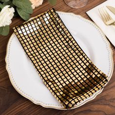 a table setting with gold and black napkins, silverware and flowers on it