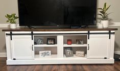 a flat screen tv sitting on top of a white entertainment center next to potted plants