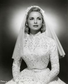 an old photo of a woman wearing a wedding dress and veil, sitting in front of a brown background