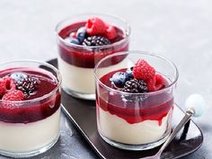 three desserts with berries and blueberries in small glass dishes on a metal tray