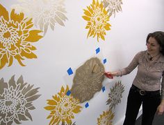 a woman painting a wall with yellow and white flowers on the wall next to her