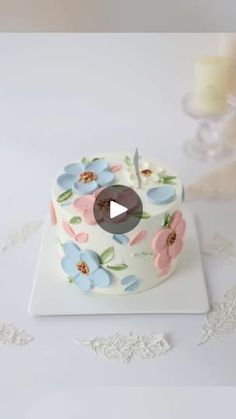 a cake with flowers on it sitting on a table next to a candle and lace doily