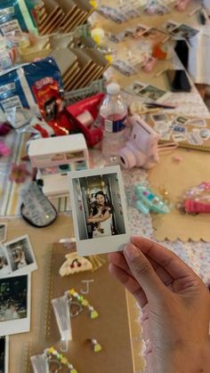 a person holding up a polaroid in front of a table full of other items