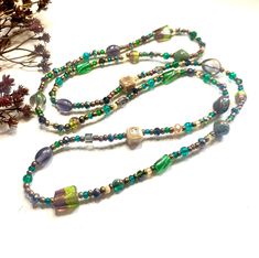 This gorgeous 42inch necklace displays gorgeous rich green, purple and teal tones. A magical forest scene with mystical colour and shimmering notes.  Adorned with glass beads in an array of shapes and finishes, it has antique bronze accents and is dotted with interesting, earthy ceramic beads. With no hassle of fastenings, simply pop this beaded necklace over your head and you are good to go! Your new handcrafted accessory will be presented beautifully in a box with soft cotton padding and a des Adjustable Green Beads Long Necklace, Adjustable Whimsical Green Necklace, Whimsical Green Beaded Necklaces As Gift, Whimsical Green Beaded Necklaces For Gift, Bohemian Long Green Necklace With Colorful Beads, Bohemian Green Long Necklace With Colorful Beads, Green Single Strand Long Beaded Necklace, Green Long Single Strand Beaded Necklace, Bohemian Long Green Necklace