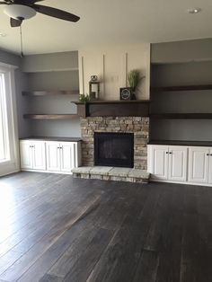 an empty living room with white cabinets and a fireplace in the center, surrounded by wood flooring