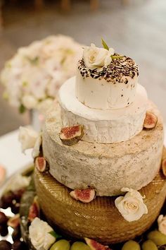 three tiered wedding cake with flowers and olives on the side, sitting on a table