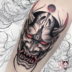 an artistic tattoo design on the leg of a man's arm with a demon mask and red eyes