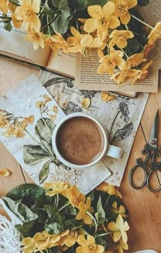 a cup of coffee sitting on top of a wooden table next to flowers and scissors