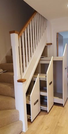 an open cabinet under the stairs in a house with wood floors and white railings