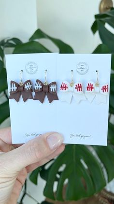 a person holding up three different colored bow clip earrings on top of a card next to a potted plant