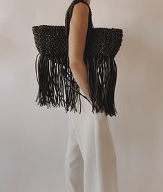 a woman in white pants holding a black bag with fringes on the front and back