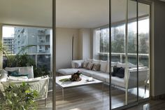 a living room filled with furniture next to a large glass window covered in plants and greenery