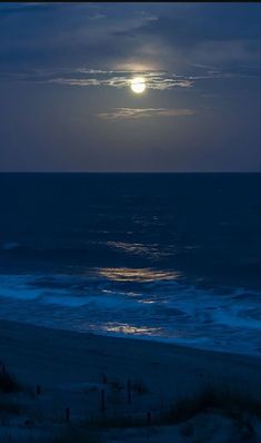 the full moon is setting over the ocean