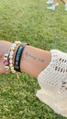 a person wearing bracelets with tattoos on their arm and wrist, in the grass