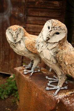 two wooden owls sitting on top of a rusted piece of wood in front of a building