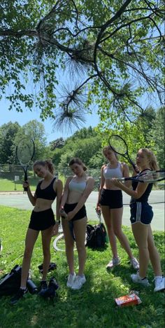 four girls are standing in the grass holding tennis rackets and wearing sports bras